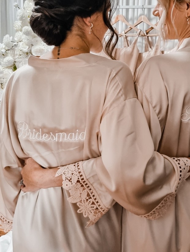 Bridesmaids wearing personalised embroidered satin robes with lace trim on the wedding morning