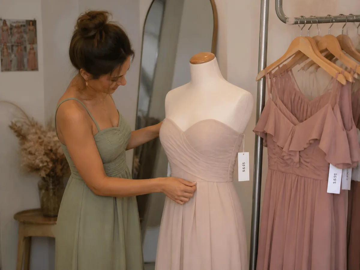 Mid-article supporting image of a person handling or selecting a bridesmaid dress or bridesmaid-party outfit on a model
